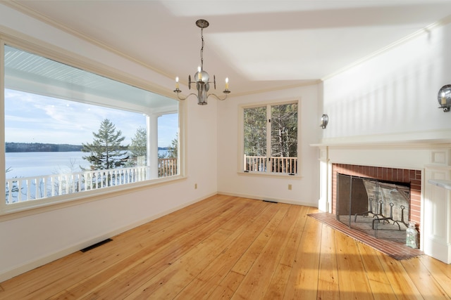 unfurnished living room with a brick fireplace, crown molding, a water view, light hardwood / wood-style flooring, and a notable chandelier