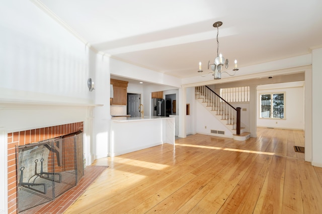 unfurnished living room featuring light hardwood / wood-style flooring, ornamental molding, a fireplace, and a chandelier