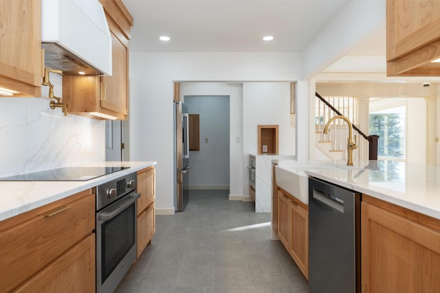 kitchen featuring sink, stainless steel appliances, tasteful backsplash, light stone counters, and premium range hood