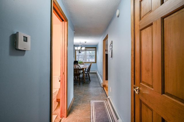 hallway with baseboard heating, a textured ceiling, and an inviting chandelier