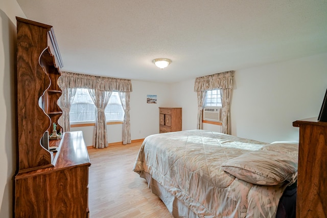 bedroom with cooling unit, light hardwood / wood-style floors, and a textured ceiling