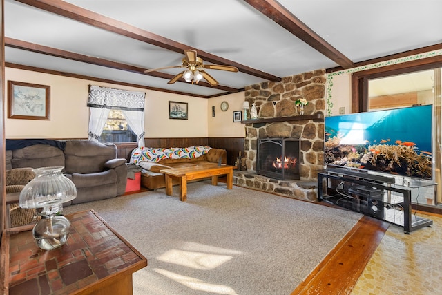 carpeted living room with beamed ceiling, a stone fireplace, ceiling fan, and wood walls