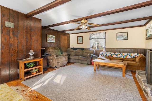 living room featuring beamed ceiling, ceiling fan, and wooden walls