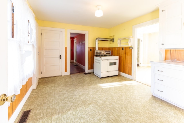 kitchen featuring white cabinets, wooden walls, and electric stove