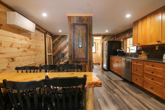 kitchen featuring appliances with stainless steel finishes, a breakfast bar, a wall mounted AC, a barn door, and wood walls