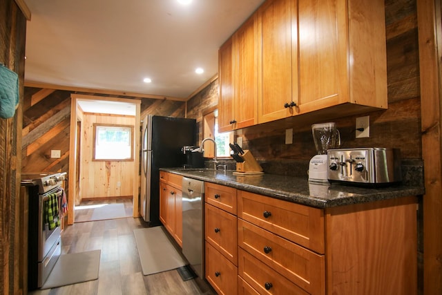 kitchen featuring wooden walls, a wealth of natural light, appliances with stainless steel finishes, and light hardwood / wood-style flooring