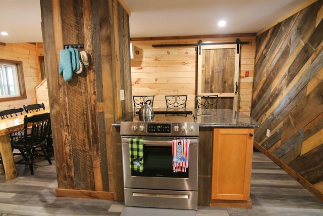 kitchen with a barn door, stainless steel electric stove, wooden walls, and dark stone countertops