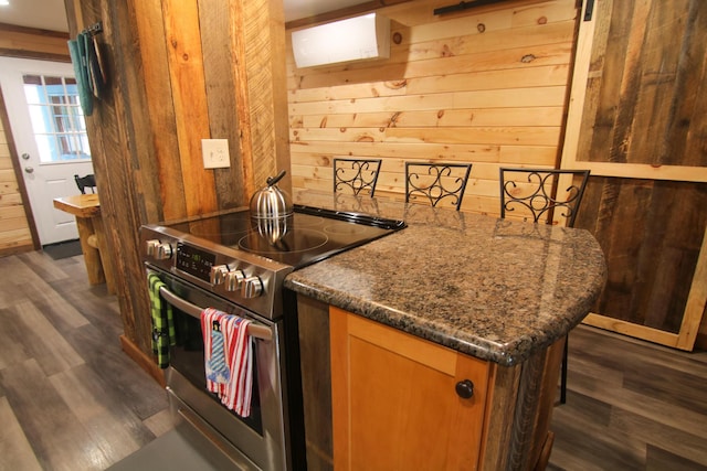 kitchen featuring dark stone countertops, dark hardwood / wood-style floors, wooden walls, and stainless steel electric range