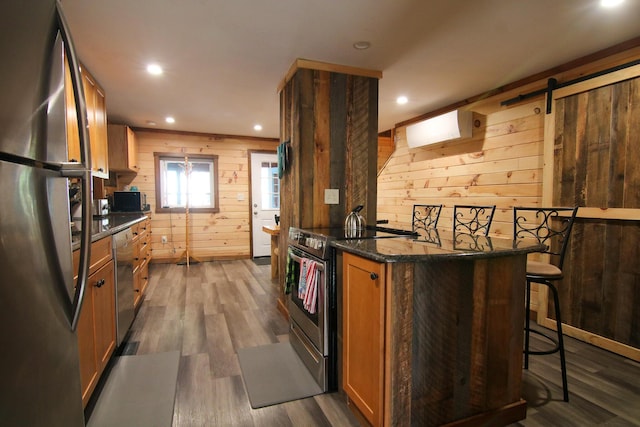 kitchen featuring dark wood-type flooring, stainless steel appliances, a kitchen breakfast bar, a barn door, and wood walls