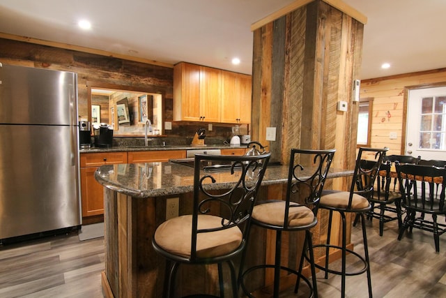 bar with dark hardwood / wood-style flooring, dark stone counters, stainless steel appliances, wooden walls, and sink