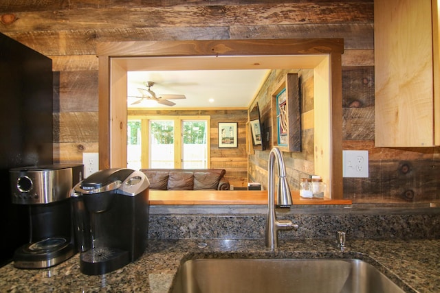 kitchen featuring stone countertops, ceiling fan, wooden walls, and sink