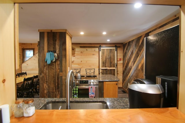 kitchen with kitchen peninsula, a barn door, stainless steel range, and wood walls