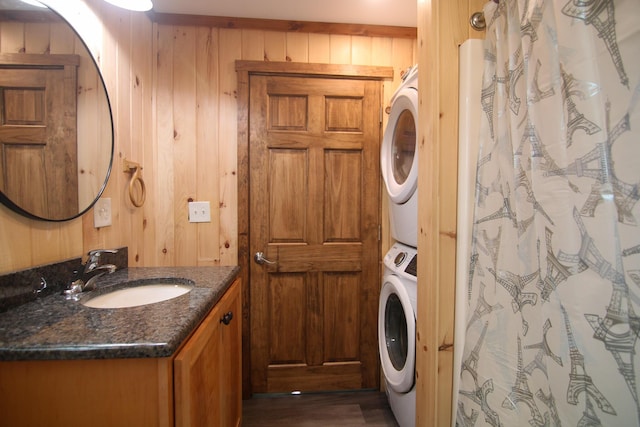 clothes washing area featuring wood walls, sink, and stacked washer / drying machine