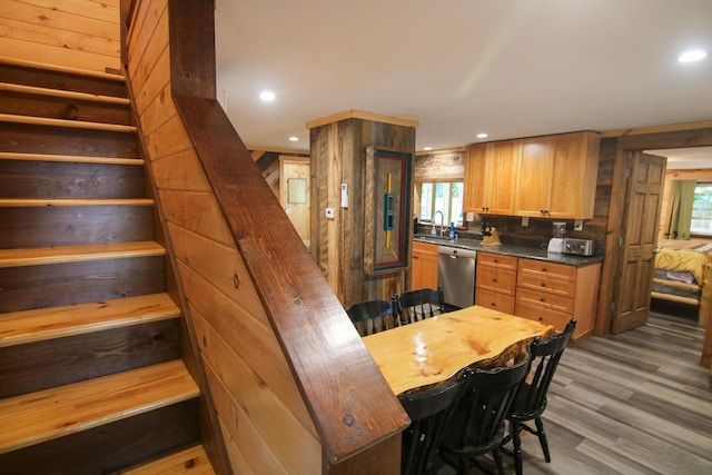 kitchen with a healthy amount of sunlight, light hardwood / wood-style flooring, stainless steel dishwasher, wood walls, and a kitchen bar