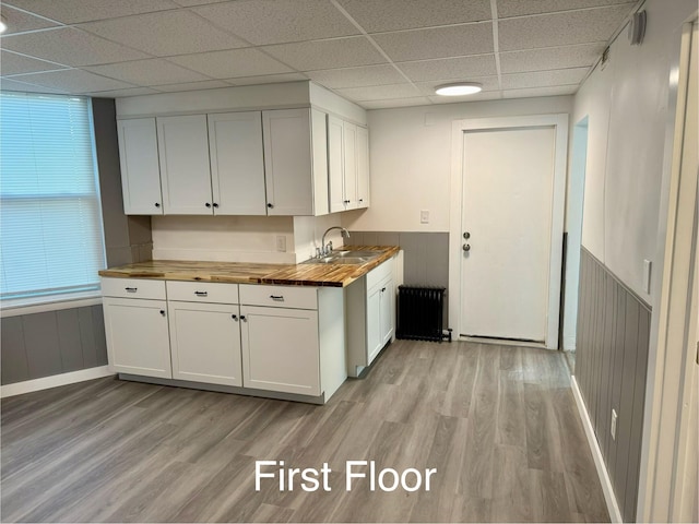 kitchen with light wood-type flooring, wood counters, radiator, sink, and white cabinetry