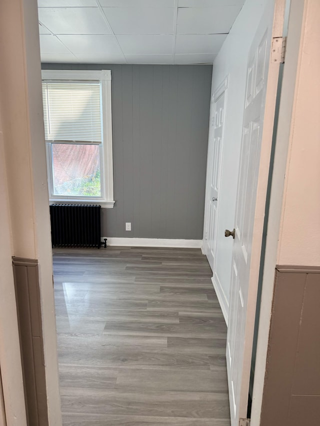 empty room with wood-type flooring, a drop ceiling, wooden walls, and radiator