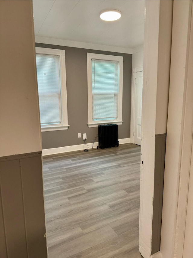 spare room featuring light wood-type flooring, ornamental molding, radiator heating unit, and plenty of natural light