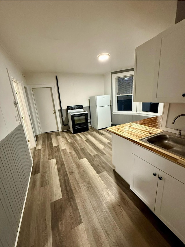 kitchen featuring white fridge, white cabinets, sink, light hardwood / wood-style flooring, and black / electric stove