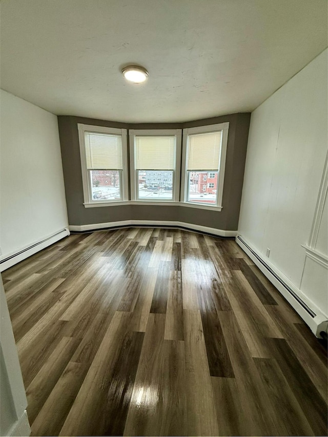 empty room with a healthy amount of sunlight, baseboard heating, and dark wood-type flooring