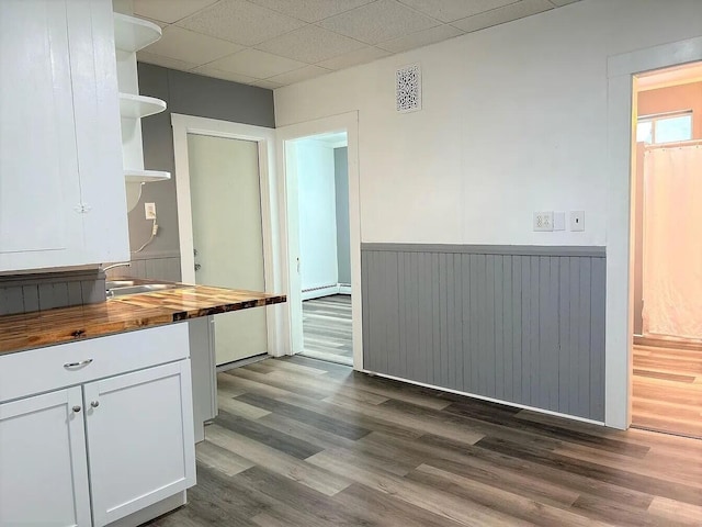 kitchen featuring dark hardwood / wood-style floors, a drop ceiling, wooden counters, baseboard heating, and white cabinetry