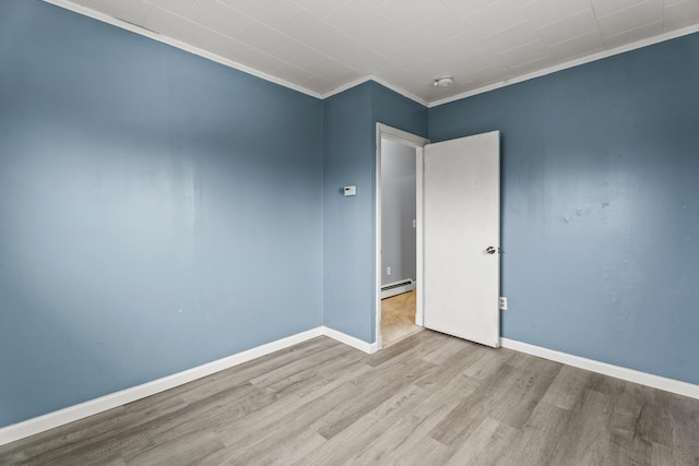 empty room featuring light hardwood / wood-style flooring, baseboard heating, and crown molding