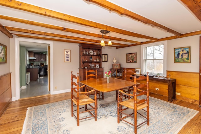 dining space with beam ceiling, light hardwood / wood-style flooring, and wooden walls