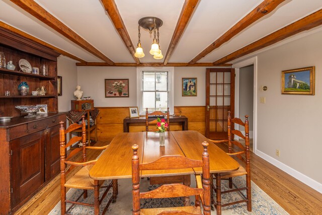 dining room featuring french doors, beamed ceiling, wood walls, a chandelier, and light wood-type flooring