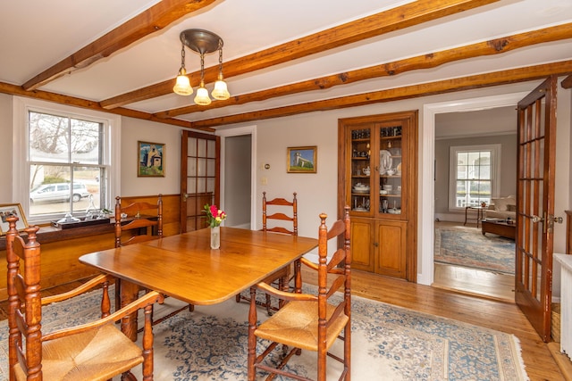 dining space featuring beam ceiling, french doors, a notable chandelier, and light hardwood / wood-style flooring