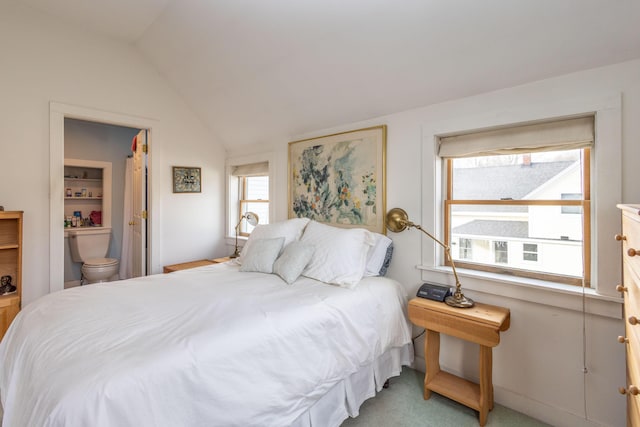 bedroom with ensuite bath, light carpet, and vaulted ceiling