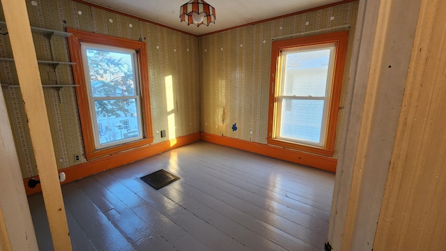 unfurnished room featuring wood-type flooring, ornamental molding, and a healthy amount of sunlight