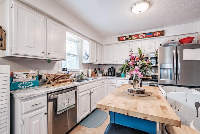 kitchen with white cabinets, sink, a textured ceiling, appliances with stainless steel finishes, and butcher block counters