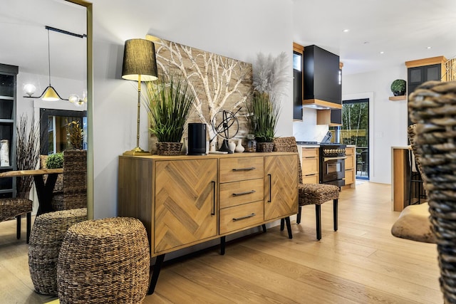 interior space with wall chimney exhaust hood, light hardwood / wood-style floors, decorative light fixtures, and stainless steel gas range