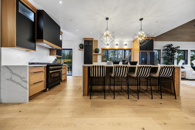 kitchen with decorative backsplash, light wood-type flooring, custom range hood, black appliances, and hanging light fixtures