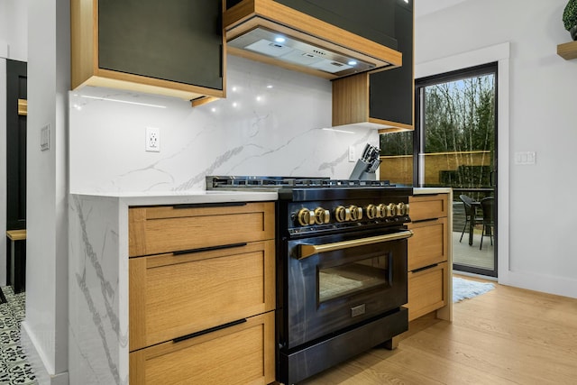 kitchen with light stone countertops, high end stove, light wood-type flooring, tasteful backsplash, and custom range hood