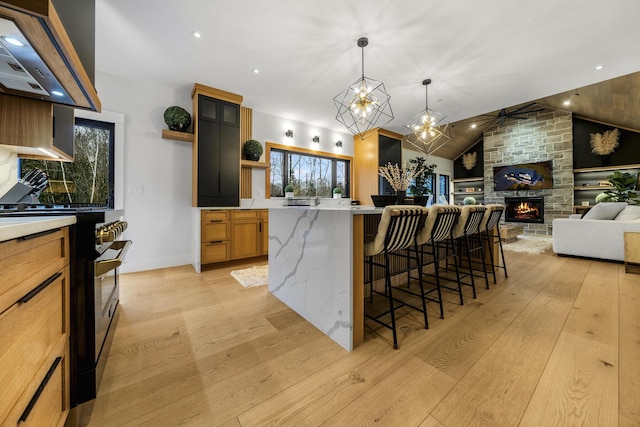 kitchen featuring a kitchen bar, vaulted ceiling, light hardwood / wood-style flooring, a stone fireplace, and plenty of natural light