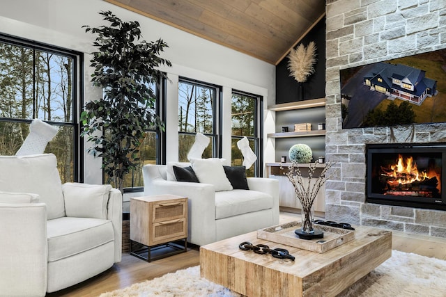 living room with a healthy amount of sunlight, a stone fireplace, light wood-type flooring, and wood ceiling