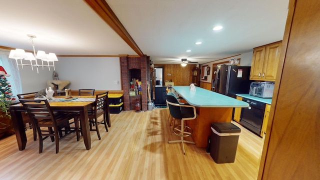 dining room with light wood-type flooring, ceiling fan with notable chandelier, wooden walls, and ornamental molding