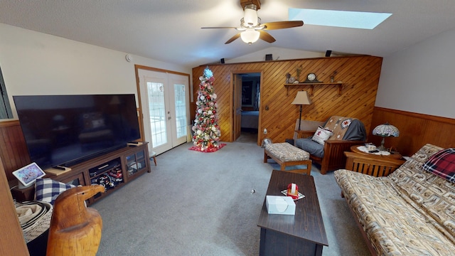 living room with wood walls, french doors, vaulted ceiling with skylight, ceiling fan, and carpet floors