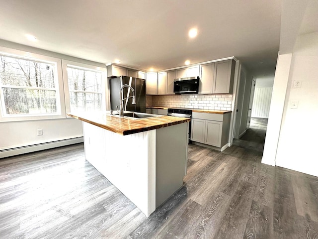 kitchen featuring gray cabinetry, stainless steel appliances, dark hardwood / wood-style flooring, wooden counters, and a center island with sink