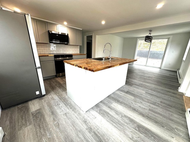 kitchen featuring wood counters, gray cabinetry, sink, stainless steel refrigerator, and an island with sink