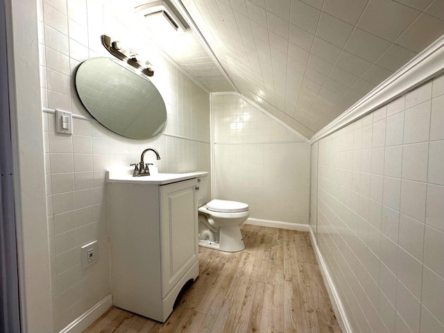 bathroom with hardwood / wood-style floors, vanity, lofted ceiling, toilet, and tile walls