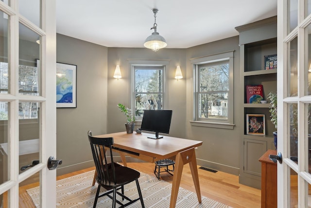 office with light hardwood / wood-style floors and french doors