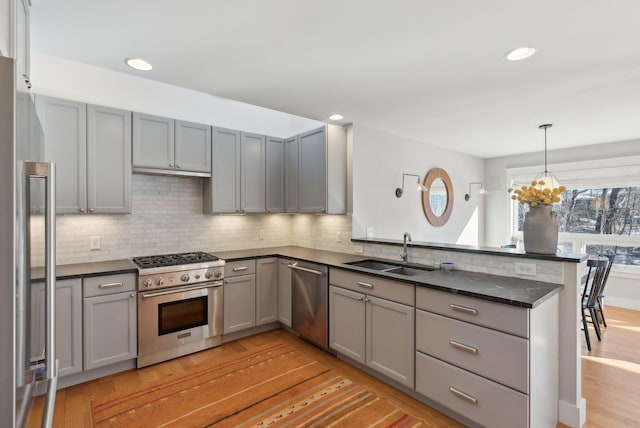 kitchen featuring kitchen peninsula, appliances with stainless steel finishes, decorative light fixtures, light wood-type flooring, and sink