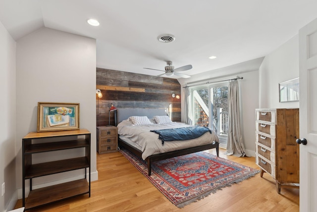 bedroom with ceiling fan, lofted ceiling, light hardwood / wood-style floors, and wood walls