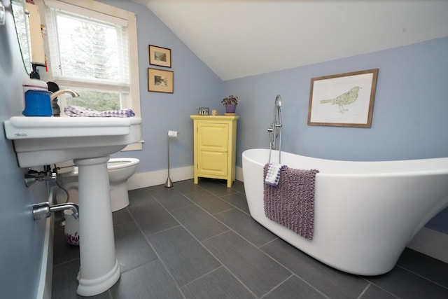 bathroom featuring toilet, lofted ceiling, a tub to relax in, and a healthy amount of sunlight