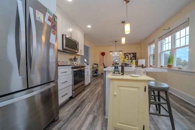 kitchen with decorative light fixtures, stainless steel appliances, a center island with sink, a breakfast bar area, and white cabinets