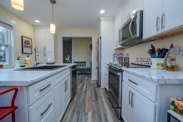 kitchen featuring pendant lighting, stainless steel appliances, hardwood / wood-style floors, white cabinetry, and sink