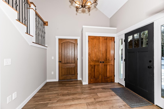 entryway with an inviting chandelier, wood-type flooring, and high vaulted ceiling