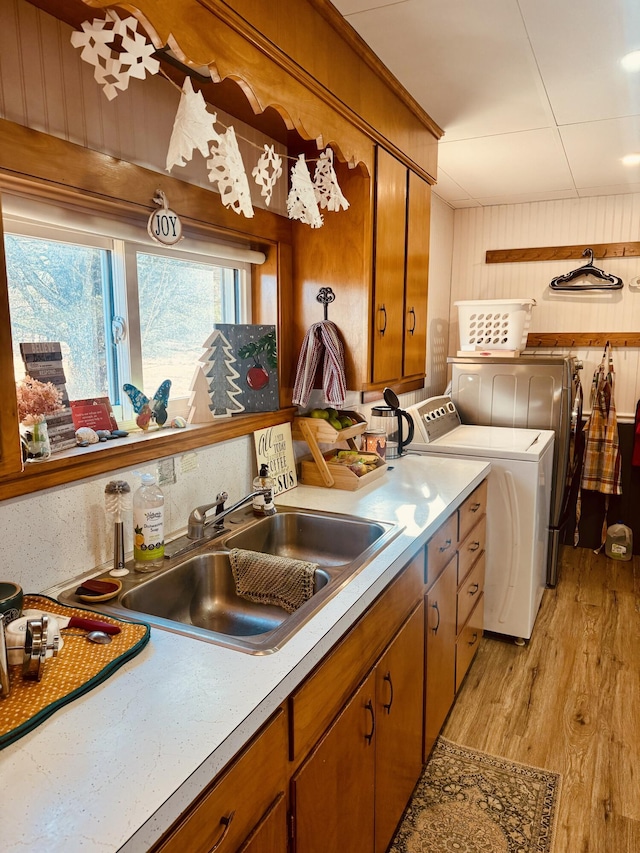 kitchen with wood walls, independent washer and dryer, light hardwood / wood-style flooring, and sink