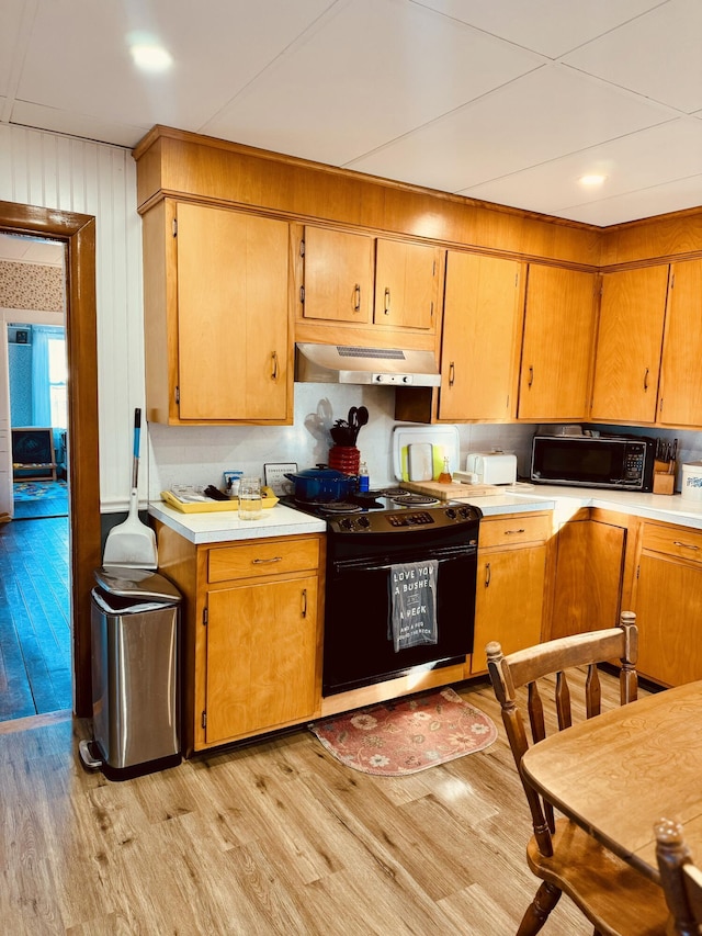 kitchen featuring black appliances, wooden walls, and light hardwood / wood-style flooring